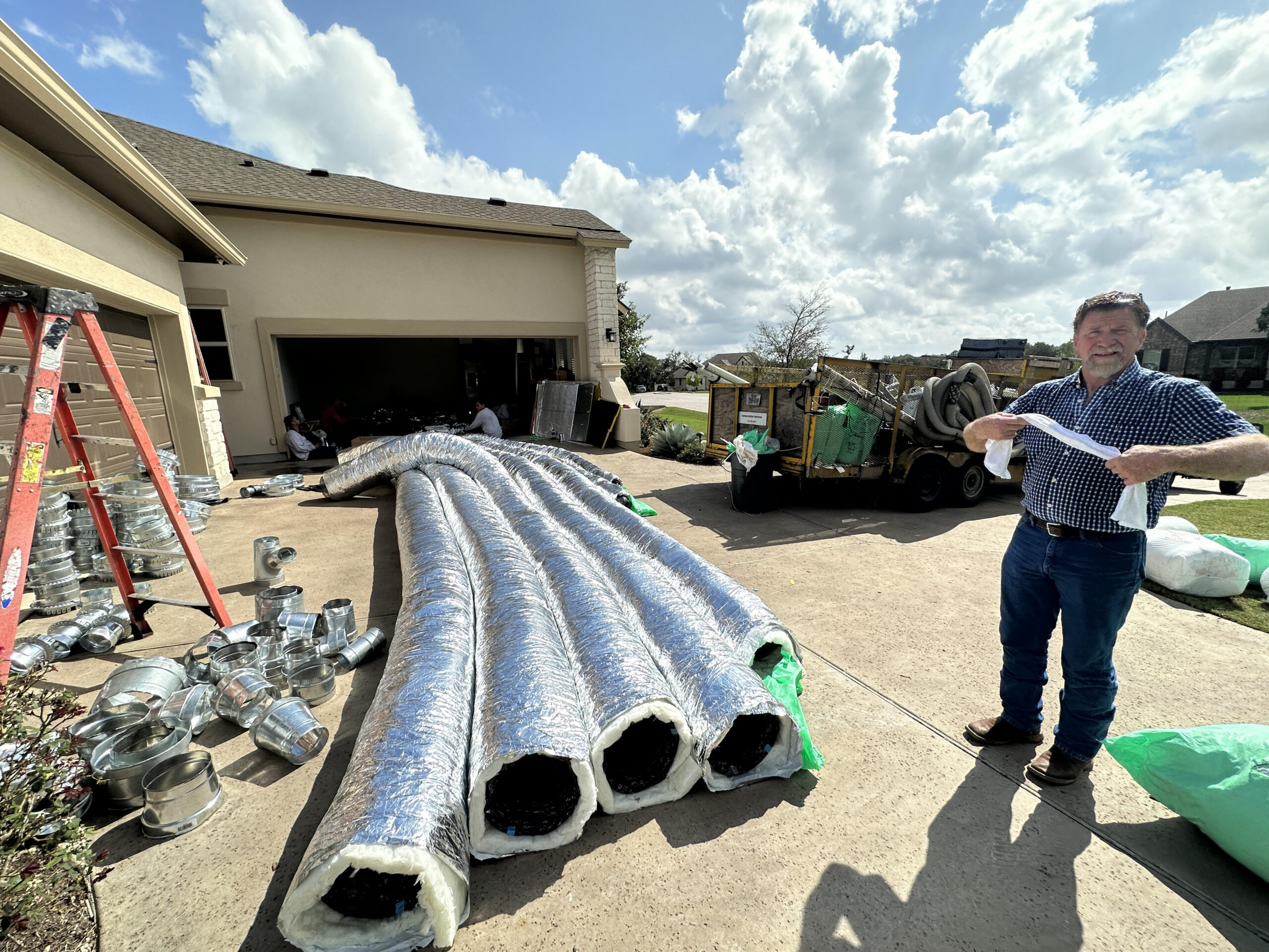 Technician inspecting replacement ductwork materials laid out on a driveway, preparing for installation at a residential property.