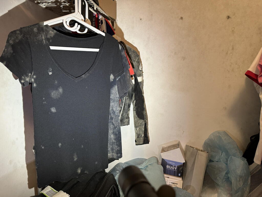 Mold-contaminated clothing hanging in a residential closet, indicating severe moisture and fungal growth issues.