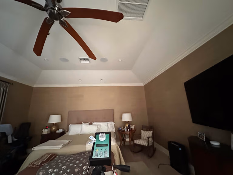Hotel-style bedroom with ceiling fan, HVAC supply vent, and indoor air quality testing equipment placed on the bed