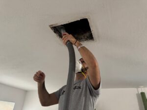 Technician performing duct cleaning by vacuuming debris from an air vent in the ceiling