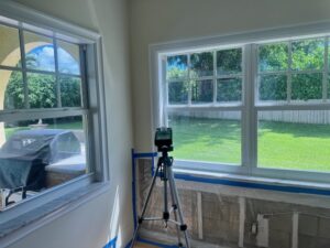 An indoor room with two large windows, featuring an air sampler on a tripod conducting mold testing during an inspection.