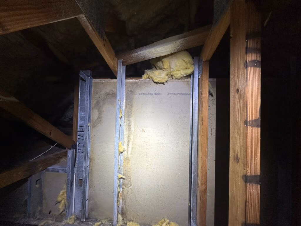 Attic wall cavity with exposed framing and insulation, showing signs of moisture exposure and potential air quality concerns.