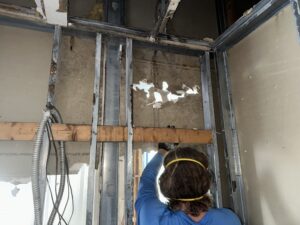 Worker performing mold remediation inside wall cavity with protective mask.