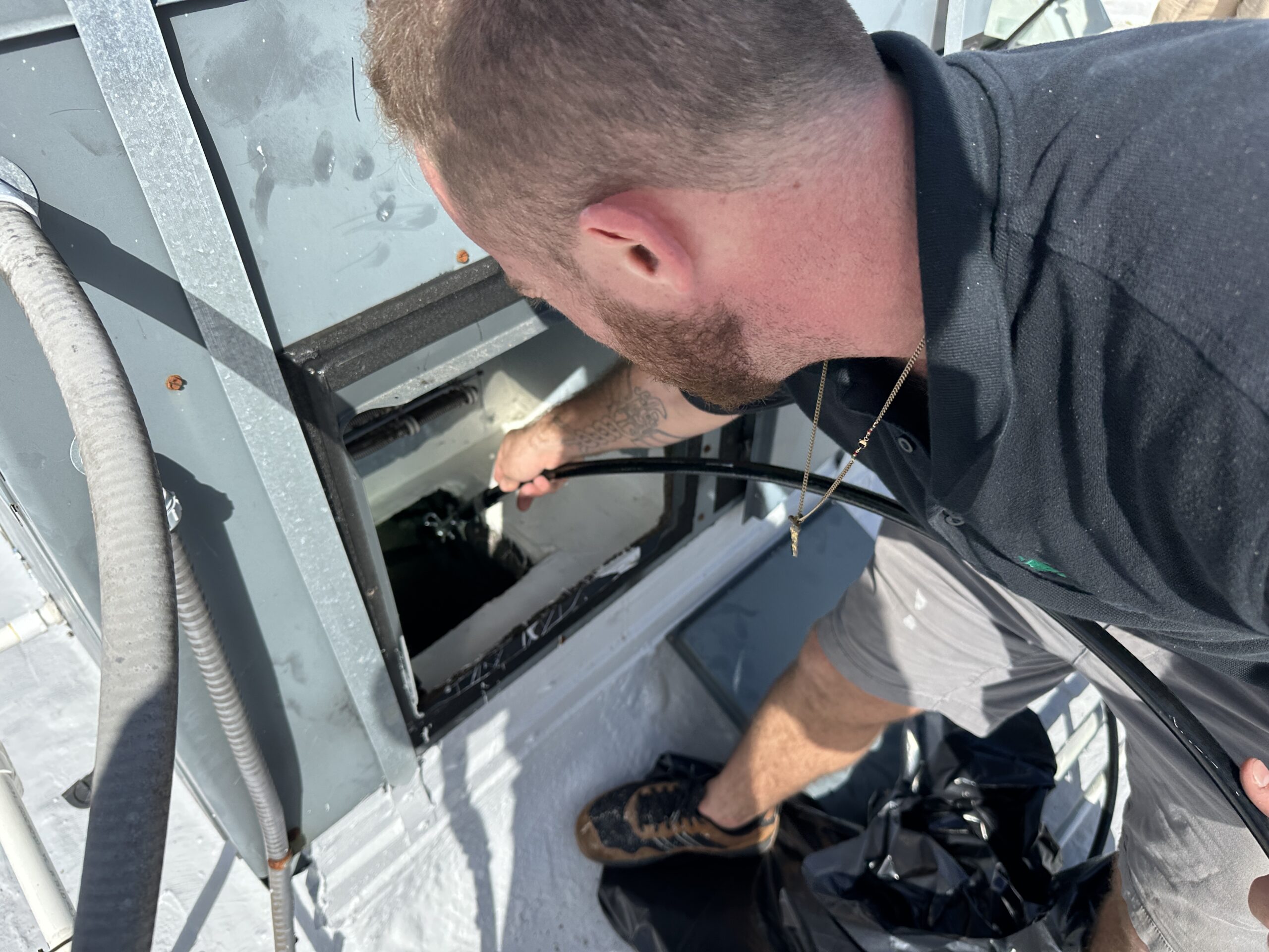 GreenFox Air Quality technician performing a detailed cleaning inside an HVAC unit on a rooftop.