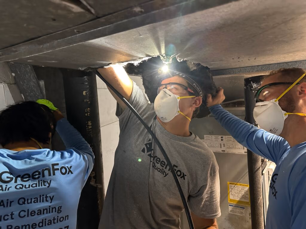 GreenFox Air Quality team members inspecting and cleaning an HVAC duct system with protective masks and tools.
