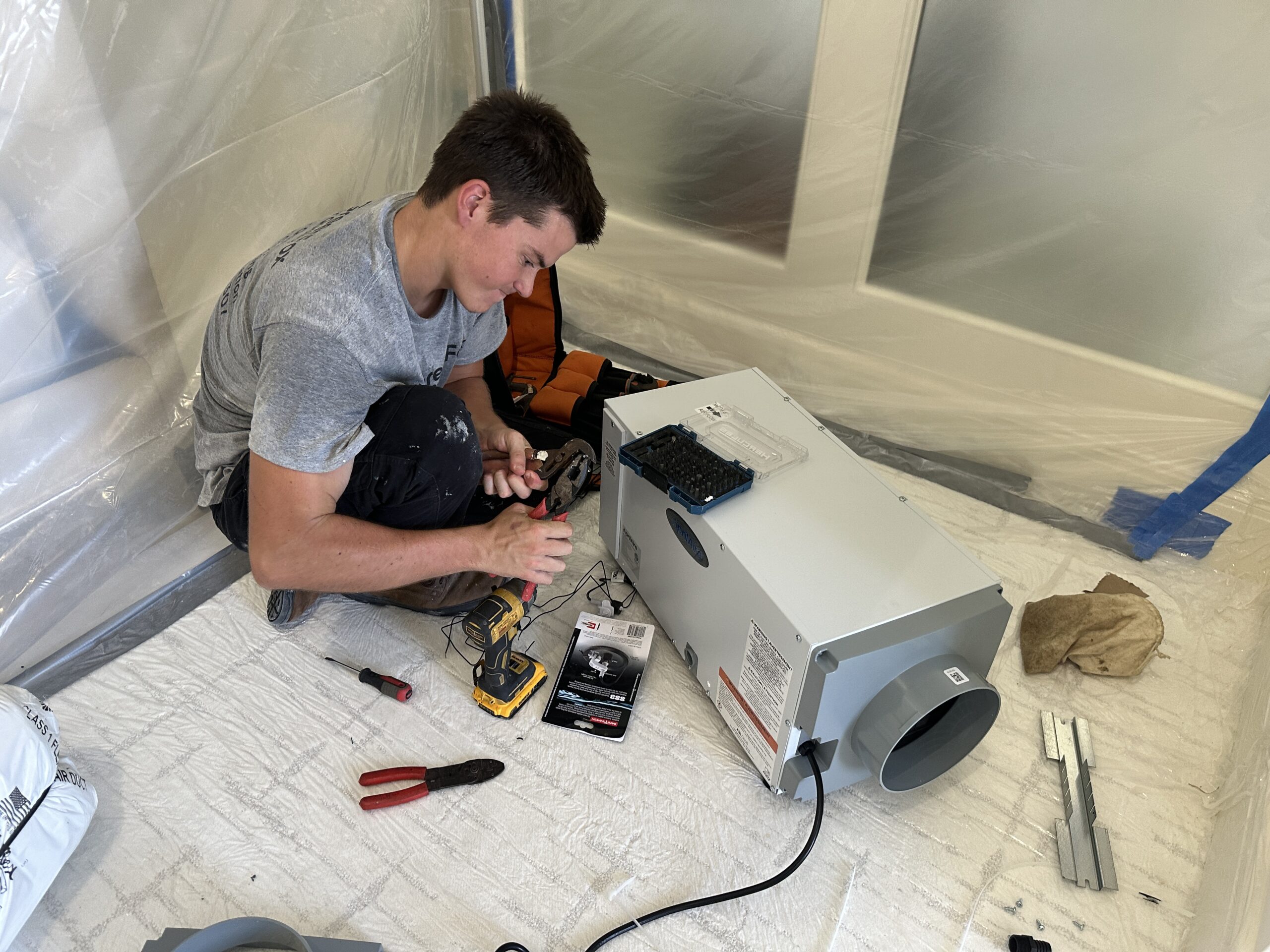 GreenFox Air Quality technician setting up a dehumidifier within a plastic containment area.