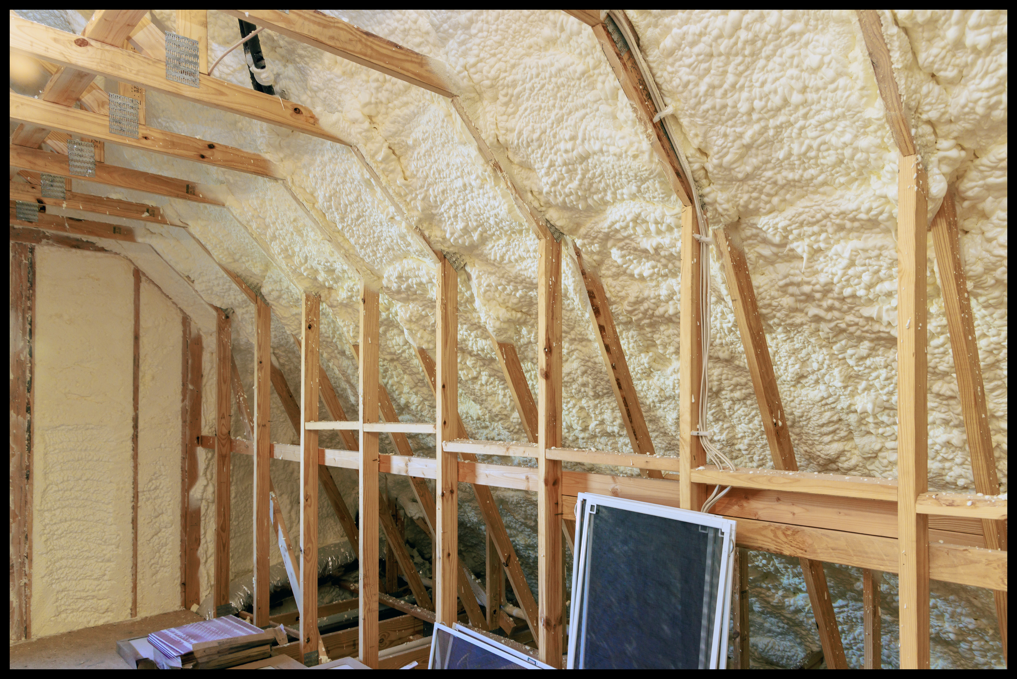 Attic space with spray foam insulation applied between wooden rafters.