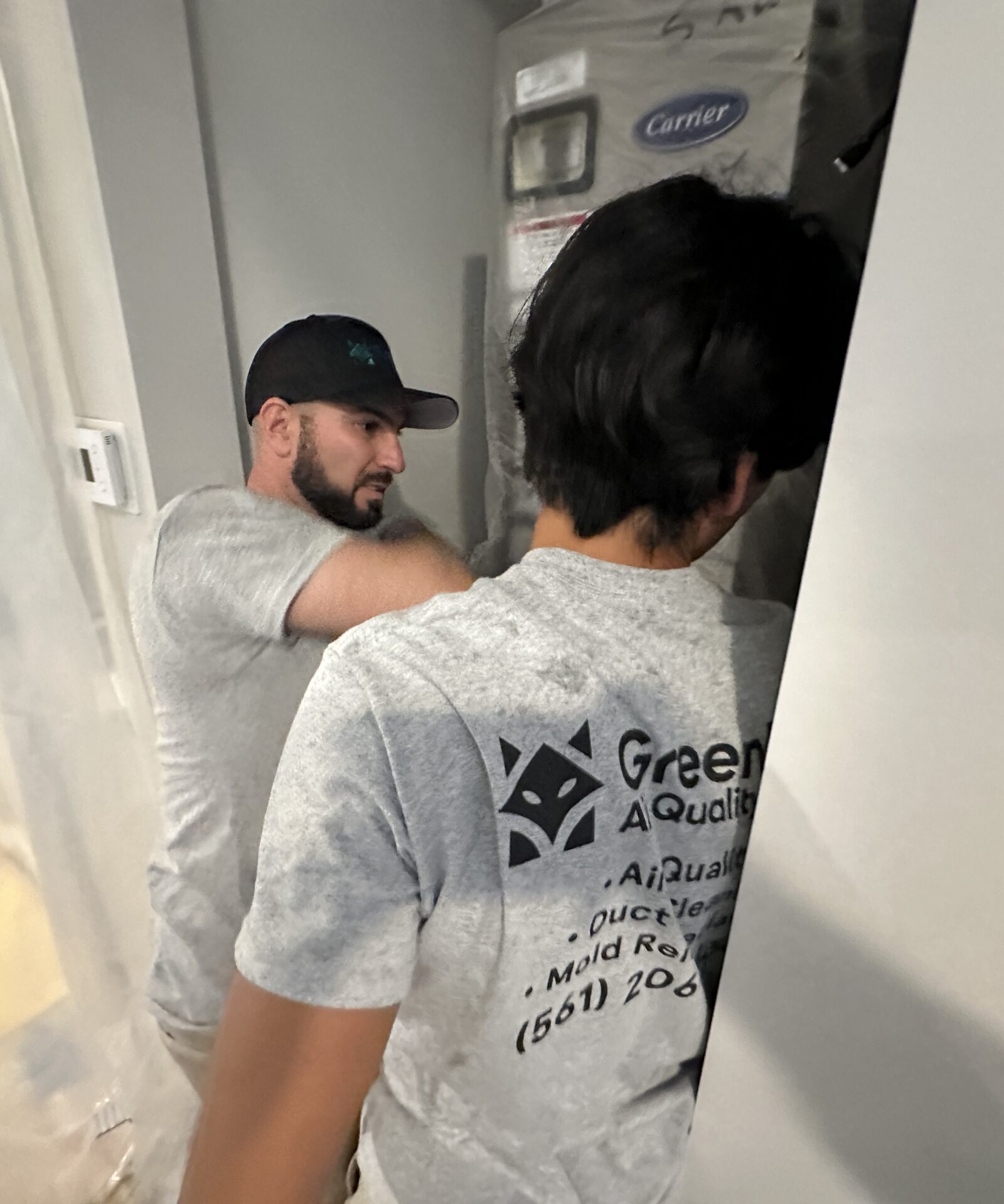 Two GreenFox Air Quality technicians inspecting an indoor HVAC system in a residential setting.