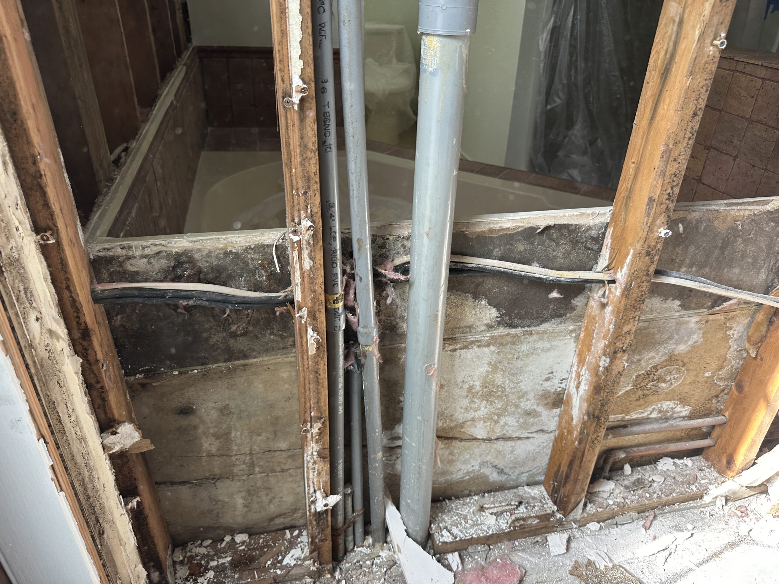 Water-damaged wall with exposed studs, pipes, and mold growth during remediation