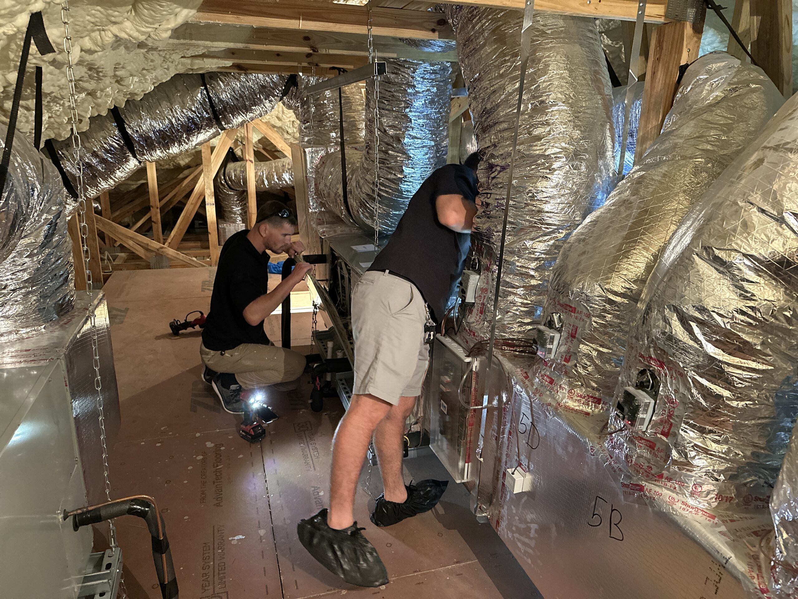 Technicians inspecting HVAC ductwork system in attic for indoor air quality