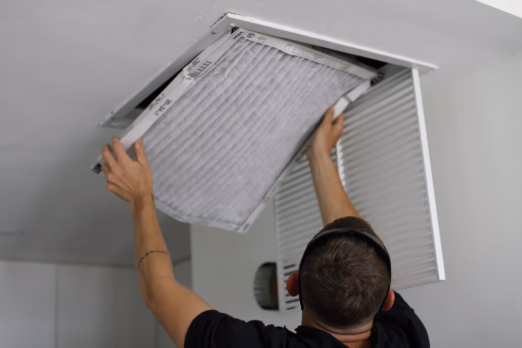 Technician installing a high-efficiency HVAC return air filter into a ceiling return grille for improved indoor air quality
