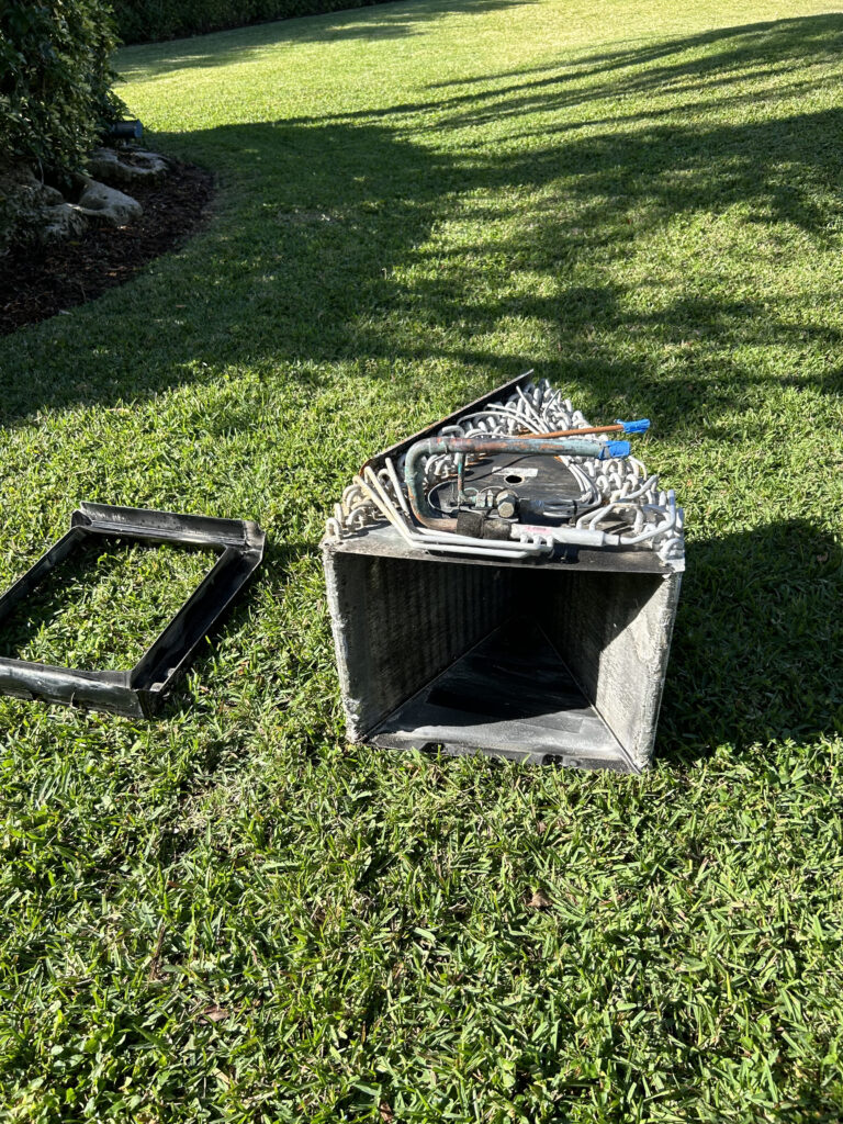 Removed HVAC coil and blower wheel assembly placed on a grassy lawn for cleaning and inspection.