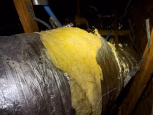 Rodent-damaged HVAC duct in attic with insulation exposed and torn open