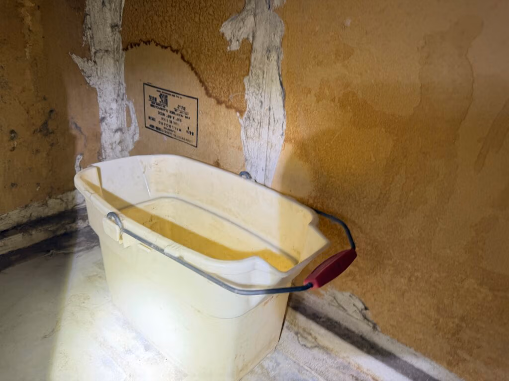 Bucket collecting condensation water beneath an HVAC air handler, showing active moisture buildup and potential ceiling damage.