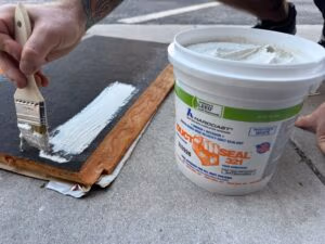 Technician applying white Hardcast duct sealant to fiberglass duct board using a brush for HVAC air sealing