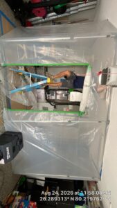 HVAC technician cleaning an air handler inside a sealed plastic containment area with negative-air filtration.